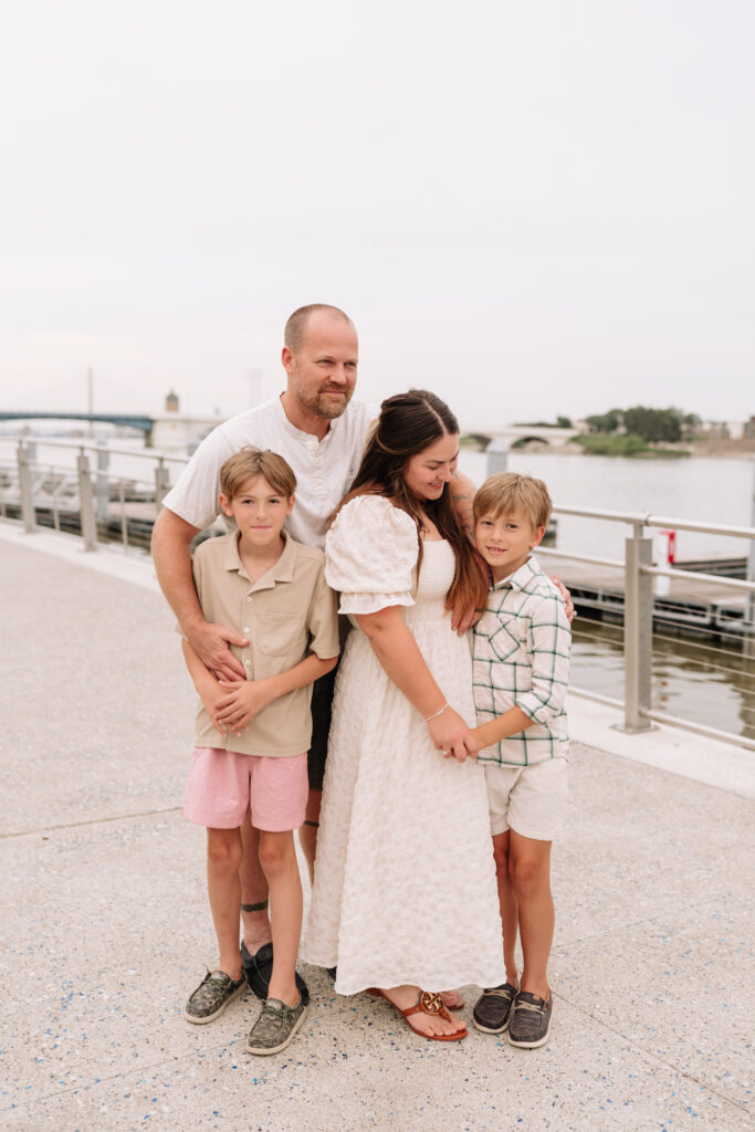 Family of five smiling during a neutral-toned outdoor photo session on a dock in Toledo, Ohio.