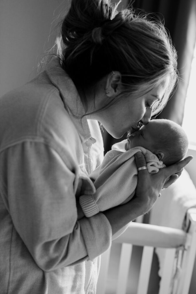 Mother holding and kissing newborn baby in a soft black and white lifestyle session in Toledo, Ohio.