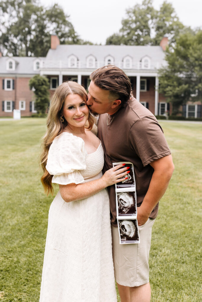 Couple sharing a kiss during pregnancy announcement in a neutral outfit on a summer day in Toledo, Ohio. what to wear to your family photos