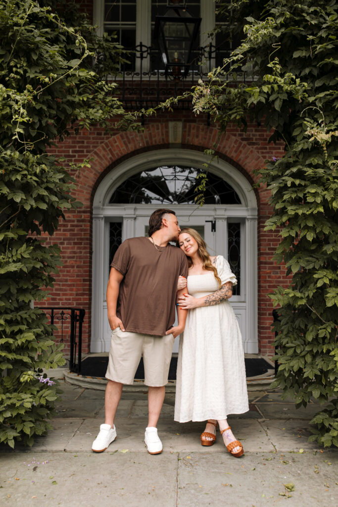  Couple announcing pregnancy in front of ivy-covered brick archway during a summer photo session in Toledo, Ohio.